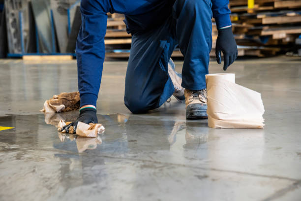 A male worker cleaning-up a slip hazard on the floor of an industrial plant.